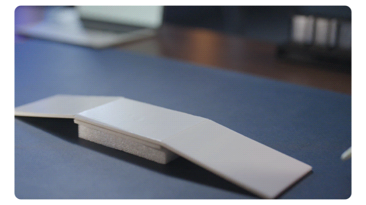 White wireless computer mouse resting on a blue desk pad or mat in a blurred office setting.