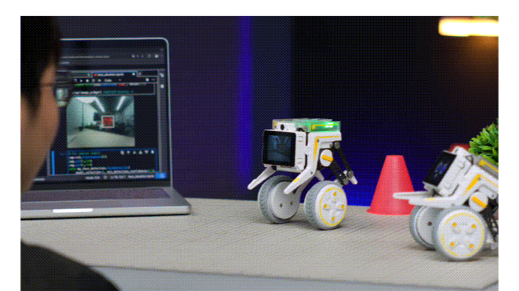Laptop screen shows code as a person programs two small wheeled educational robots on a table.