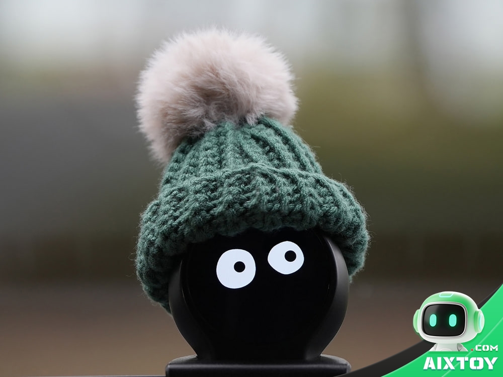 Close-up of the TOOOONY in-car AI ball wearing a knitted green beanie with a pom-pom and a pair of cartoon eyes on its circular screen